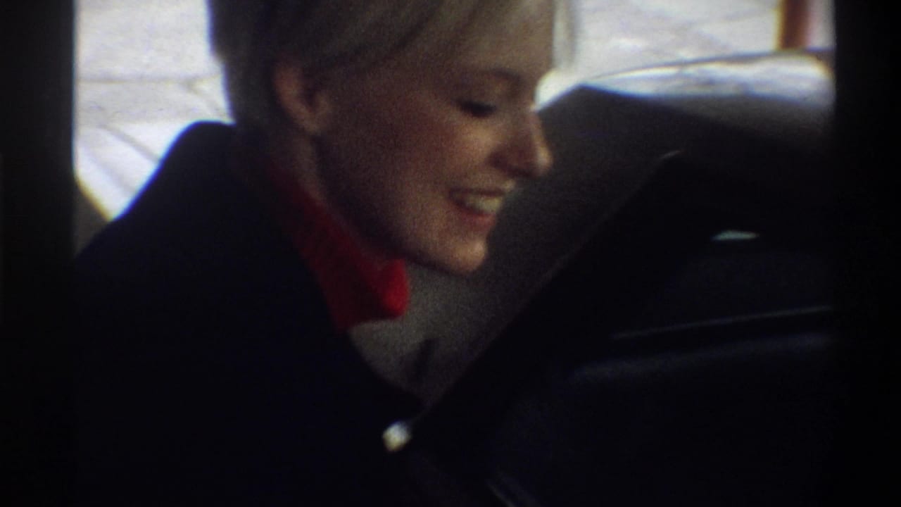 Close-up of a smiling woman with short blonde hair in a dark coat and red turtleneck, filmed on 8mm in Gainesville, Florida, circa 1974.