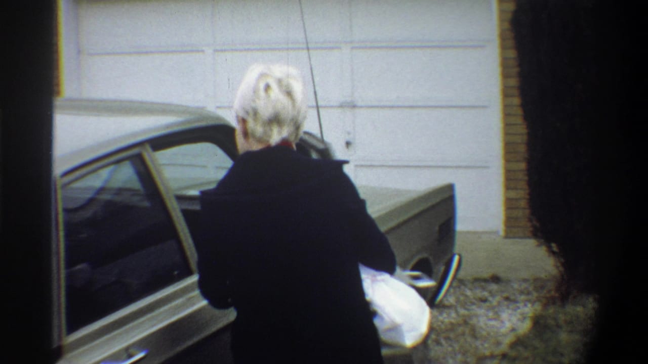 Woman in dark coat exits a 1970s olive-gold sedan holding what appears to be a bundled infant, suburban Gainesville FL, circa 1974.