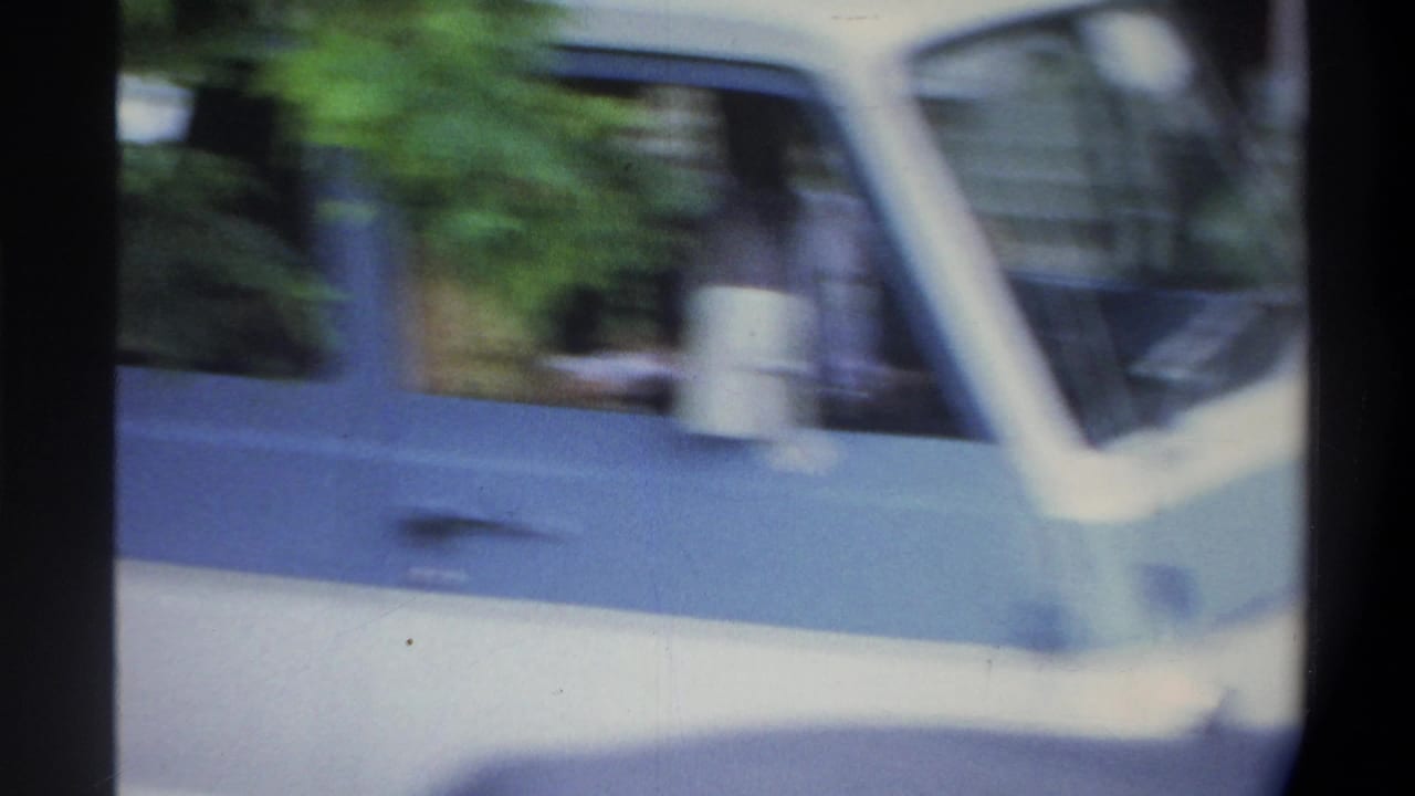 Heavy motion blur from a handheld camera pan following a cream sedan; trees and street are smeared across the frame, Gainesville Florida area, circa 1974.