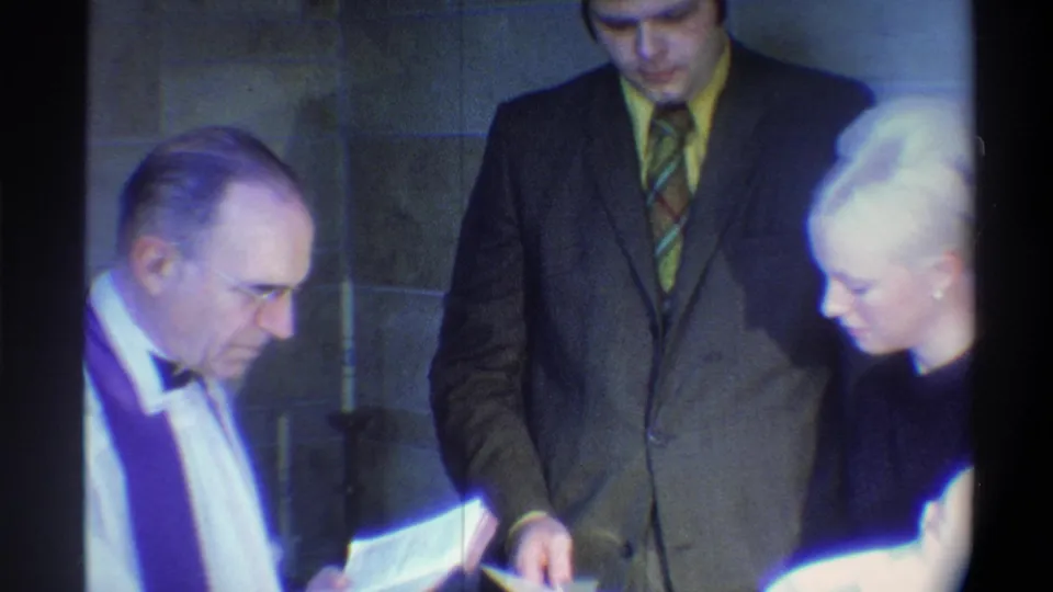 Officiant in white alb and purple stole reads liturgy beside a groom in 1970s attire; 8mm home movie, Gainesville, Florida, 1974.