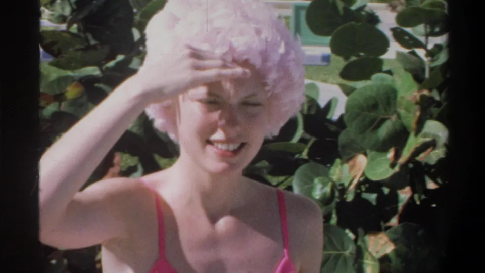 Young woman in pink string bikini and ruffled swim cap smiling and shielding eyes, outdoor pool setting, Gainesville Florida area, circa 1974.