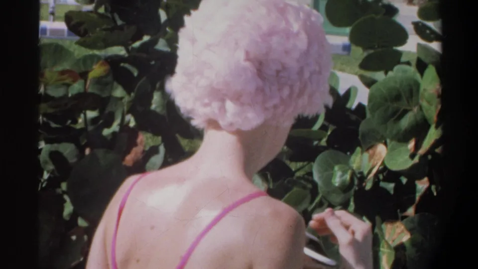 Rear view of young woman in pink string bikini and ruffled pink swim cap turning away outdoors, lush tropical vegetation, Gainesville Florida area, circa 1974.