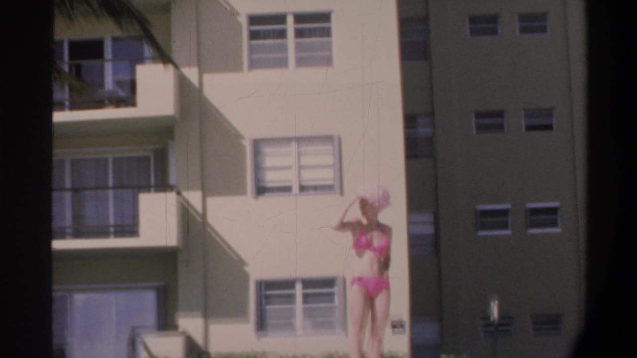 Woman in pink bikini adjusts her wide-brim hat while standing before a multi-story Florida apartment building with balconies, circa 1974.