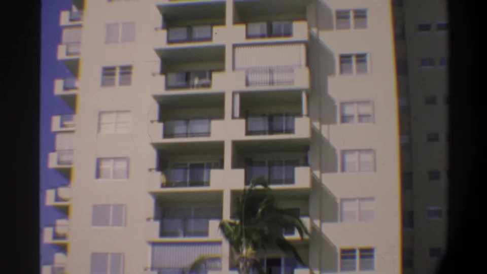 Beachfront high-rise building with balconied facade and palm tree, filmed on Super 8 in Florida, c. 1974.