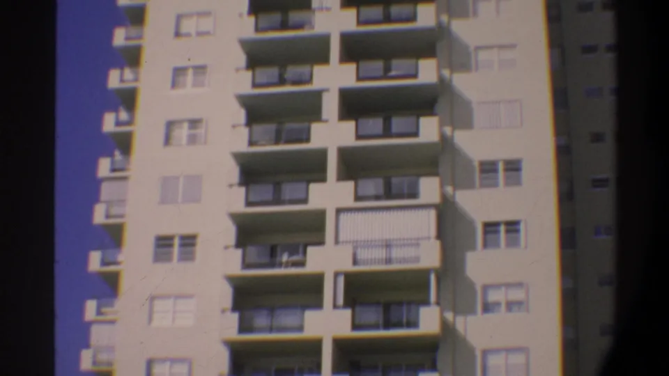 Beachfront high-rise facade with balconies and palm trees, Super 8 home movie, c. 1974 Florida.