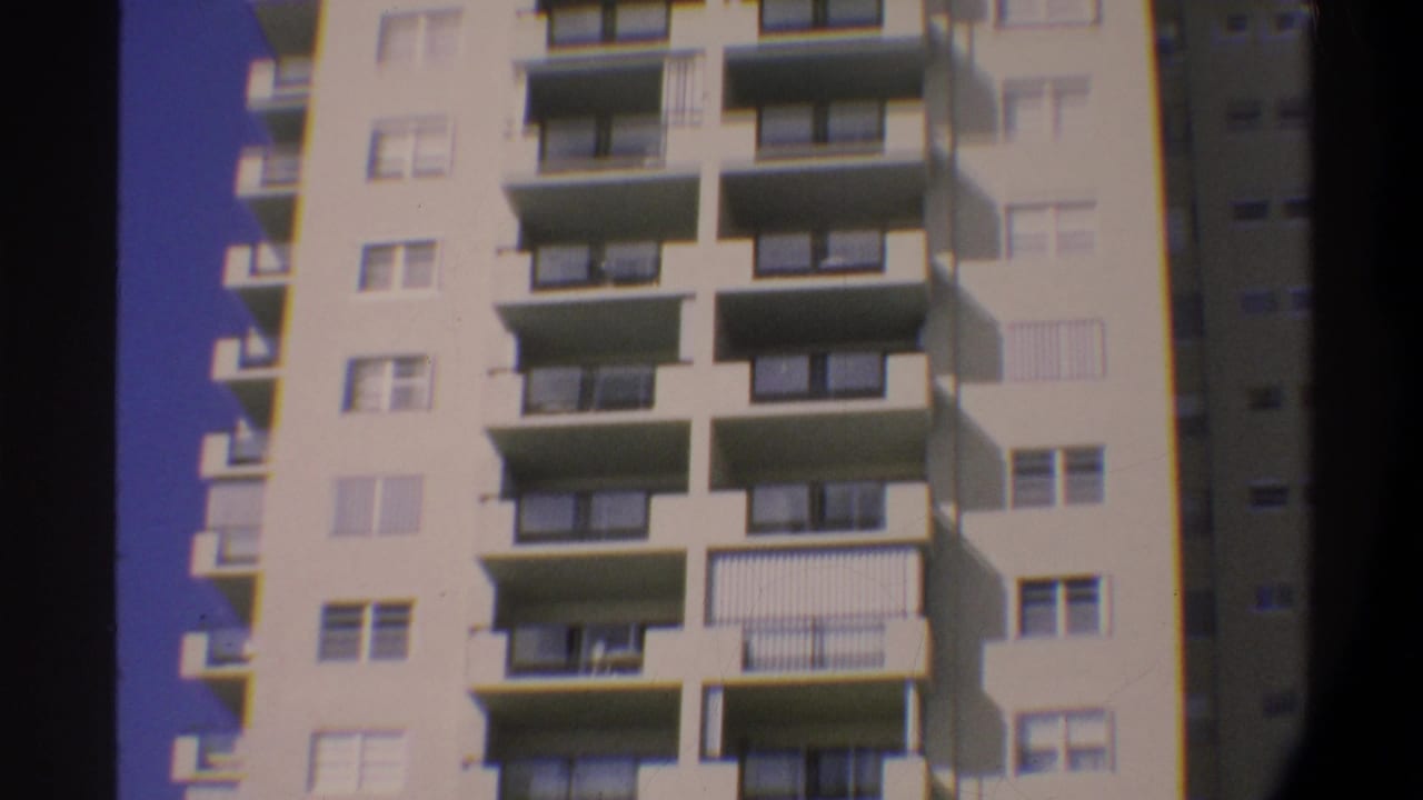 Multi-story condominium building in Gainesville, Florida, circa 1974, filmed on 8mm; cream facade with horizontal balconies and metal railings against deep blue sky.