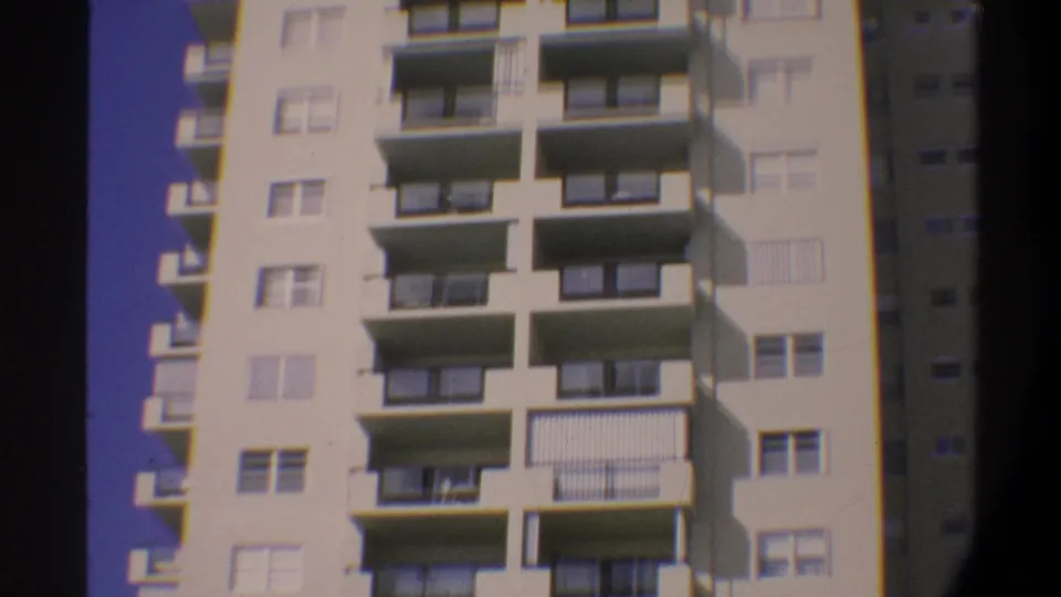 Multi-story condominium building in Gainesville, Florida, circa 1974, filmed on 8mm; cream facade with horizontal balconies and metal railings against deep blue sky.