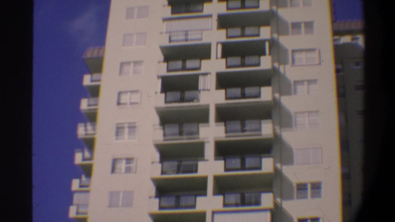 Continuing upward tilt on a multi-story Gainesville, Florida condominium, circa 1974; cream facade and repeating balcony pattern against saturated blue sky.
