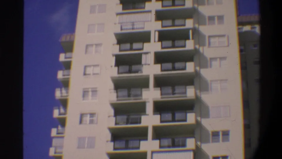 Continuing upward tilt on a multi-story Gainesville, Florida condominium, circa 1974; cream facade and repeating balcony pattern against saturated blue sky.
