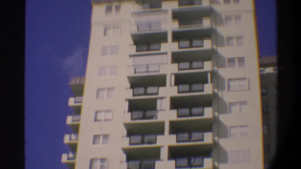 Upper floors of a multi-story Gainesville, Florida condominium, circa 1974; pale blue sky visible as the 8mm camera approaches the building's upper third.