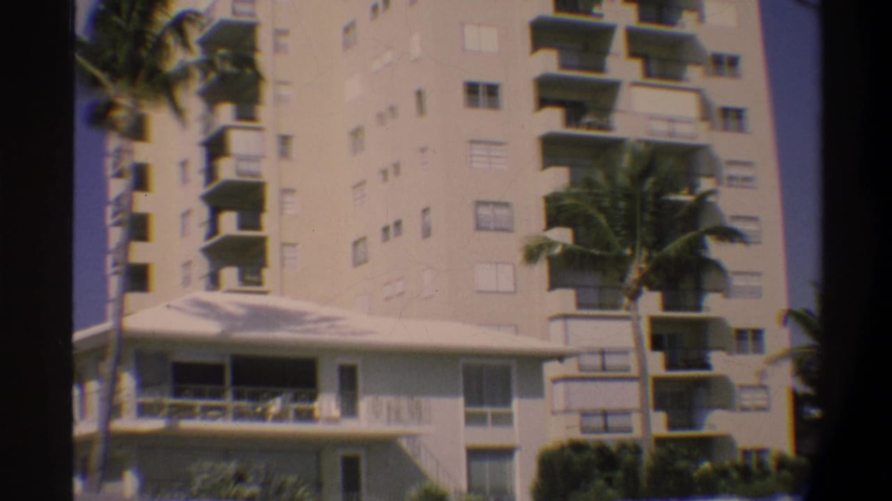 8mm home-movie frame of a multi-story Florida residential or resort building with repeated balconies and flanking palm trees, Gainesville area, circa 1974.