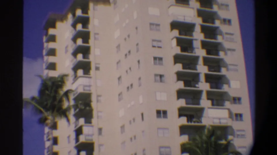 8mm home-movie frame of the upper floors of a Florida high-rise; balconies fill most of the frame with palm fronds at right and open sky at left, circa 1974.