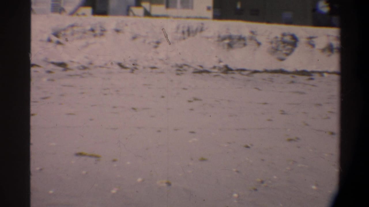 Sandy ground beside a low concrete wall, shot on 8mm film circa 1974 in Florida; strong film grain and pinkish color fade throughout.