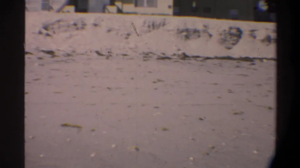 Sandy ground beside a low concrete wall, shot on 8mm film circa 1974 in Florida; strong film grain and pinkish color fade throughout.