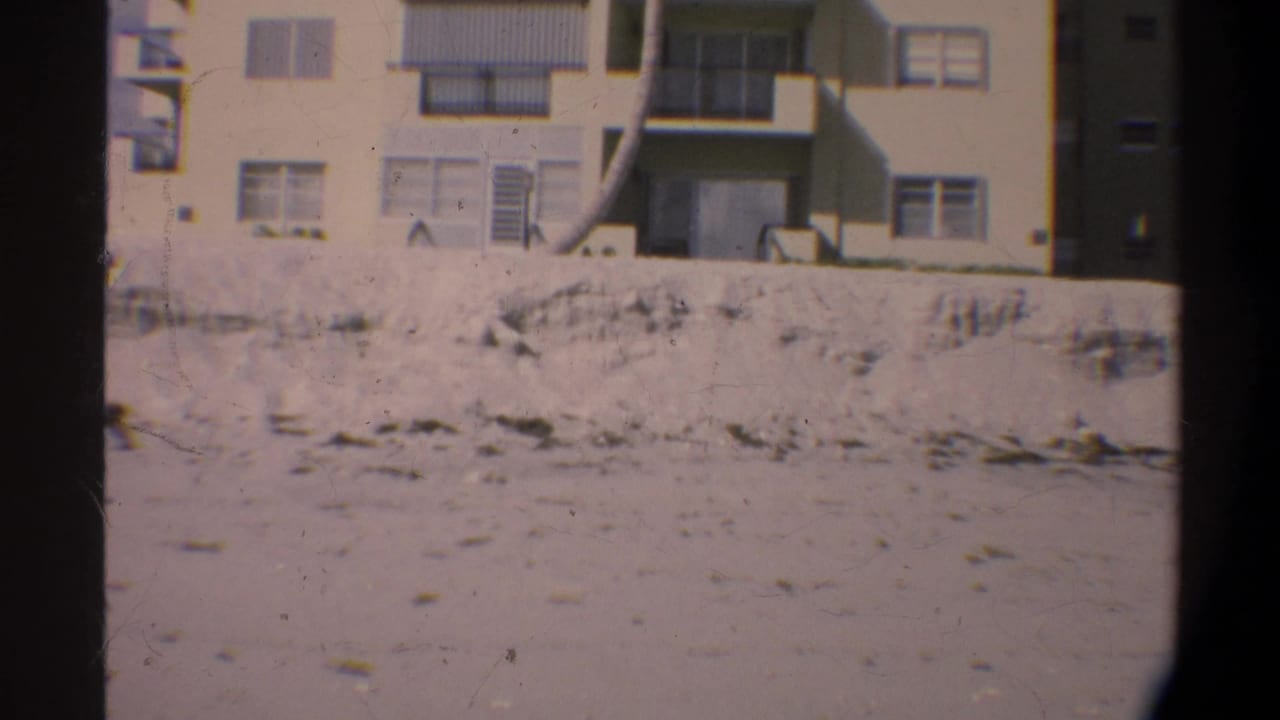 Sandy lot with low wall and the facade of a multi-story apartment building visible at upper right.