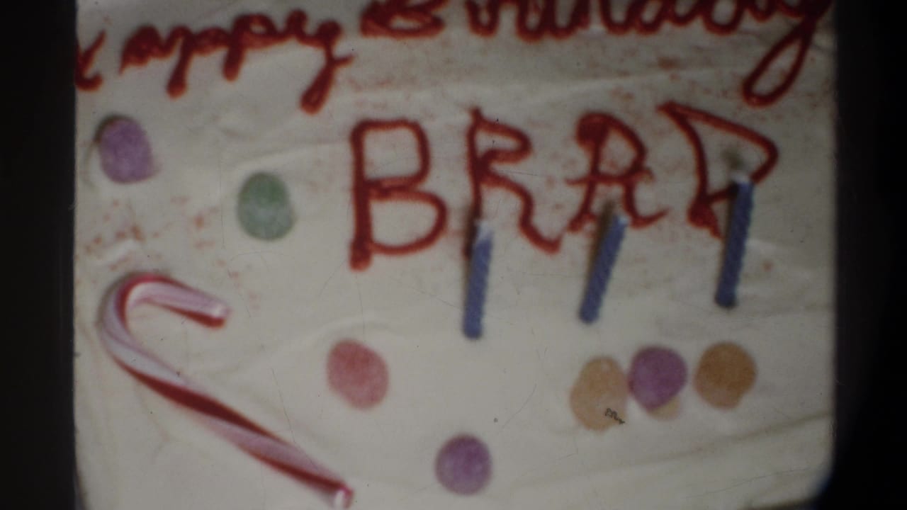 Final 8mm frame circa 1974, Gainesville FL — sheet cake with 'Happy Birthday BRAD' in red icing, blue birthday candles, a candy cane, and colorful gumdrop decorations.