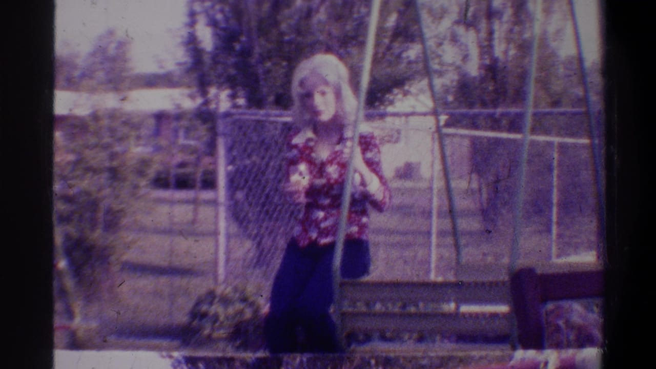 Young woman in mid-1970s floral blouse and wide-leg trousers standing beside a swing set in a suburban backyard, Gainesville, Florida, circa 1974; 8mm film with purple color cast.