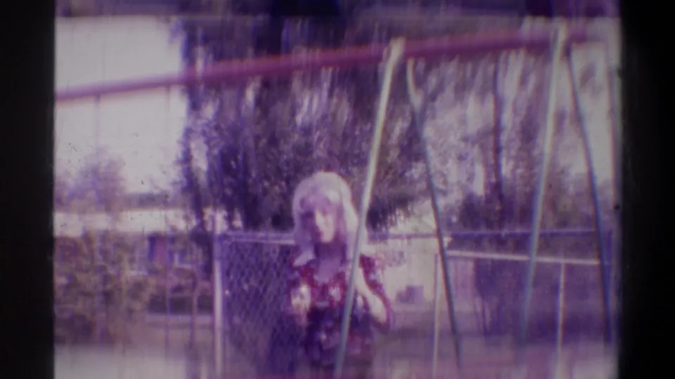 Young woman seated on a backyard swing in a suburban yard, circa 1974 Gainesville, Florida; swing set metal frame visible; 8mm footage with color shift and grain.