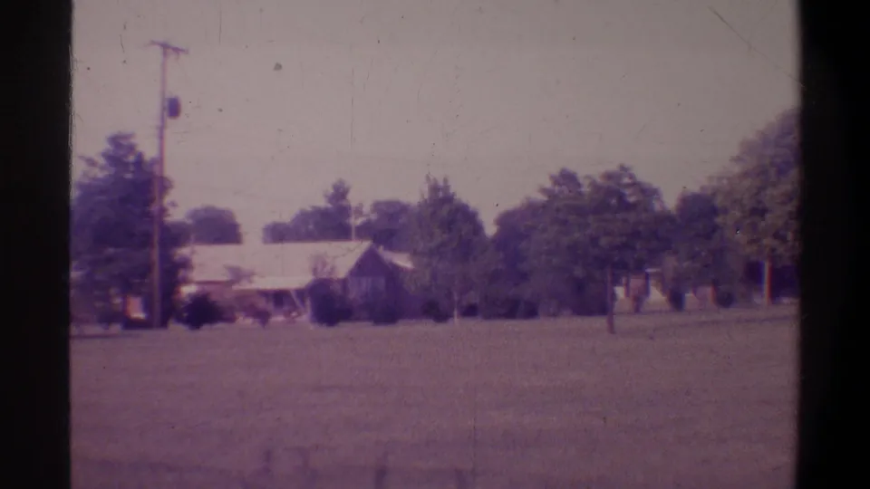 End-of-pan frame of a suburban residential scene in Gainesville, Florida, circa 1974, with house, utility pole, and tree canopy across a wide lawn on 8mm.