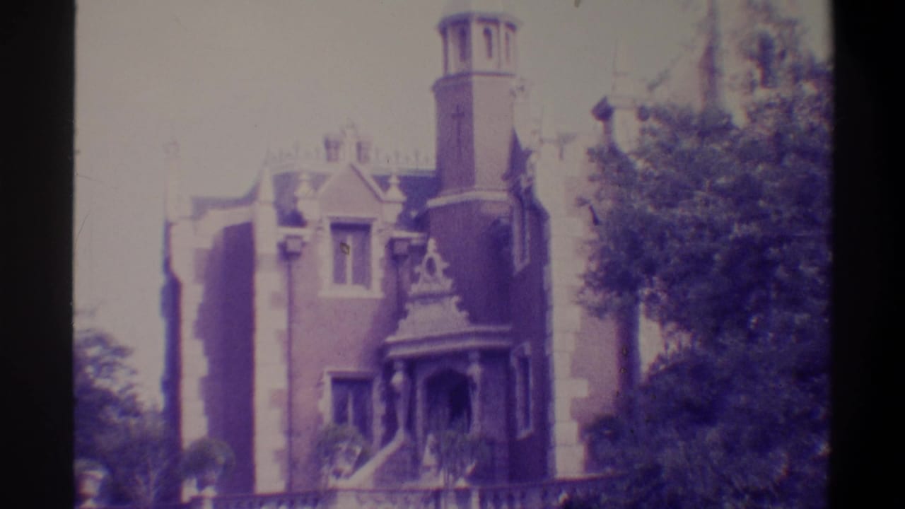 Same Gothic Revival brick building, tower prominent at upper right, ornate entry porch and steps visible at lower left; purple-toned 8mm footage.