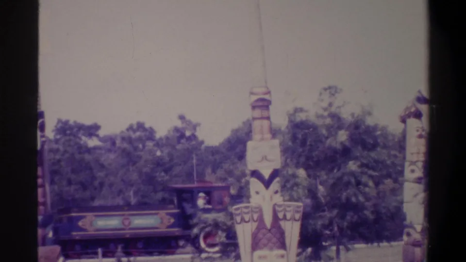 Close view of a miniature park train with a decorative painted front panel alongside totem-style columns, Gainesville Florida area, 1974