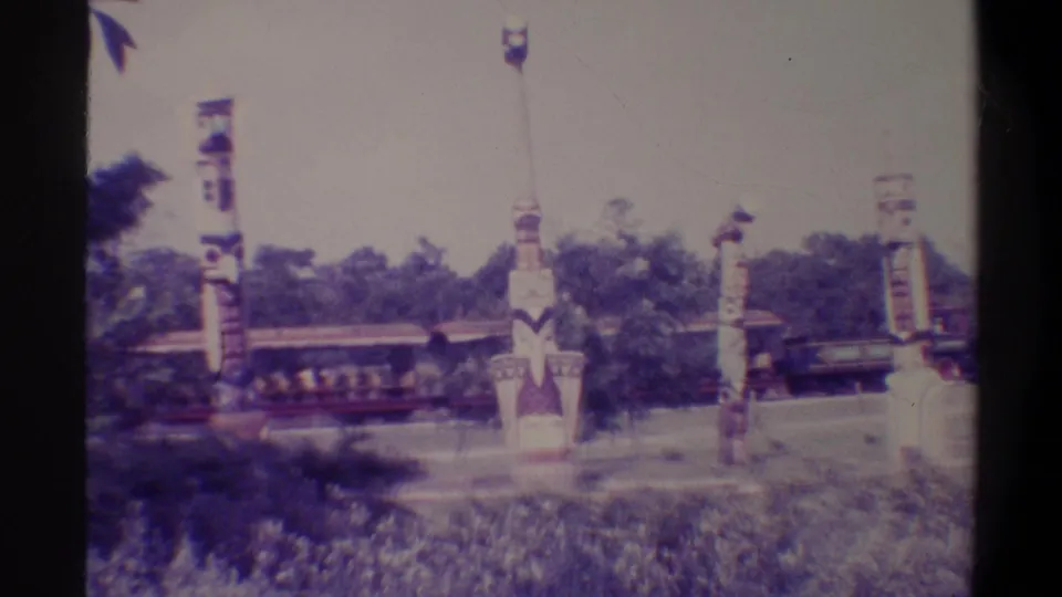 Painted totem poles at what appears to be a Florida tourism attraction with open train cars behind; 8mm film grain and camera movement are visible throughout, c. 1974.