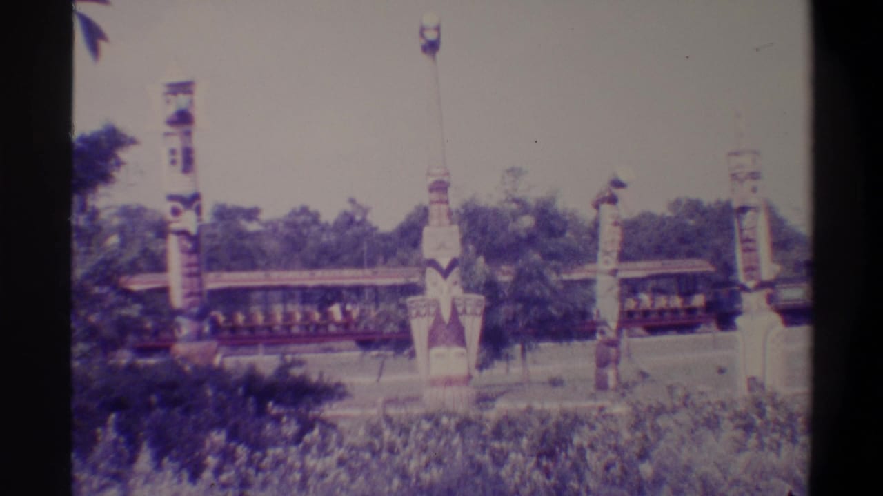 8mm frame from what appears to be a Florida family attraction, circa 1974, showing a slow ride train passing carved totem-style poles against dense foliage.