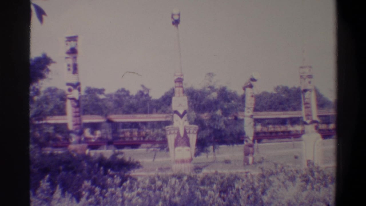 8mm frame circa 1974 showing a ride train mid-pass behind decorative totem-style poles at what appears to be a Florida family attraction.