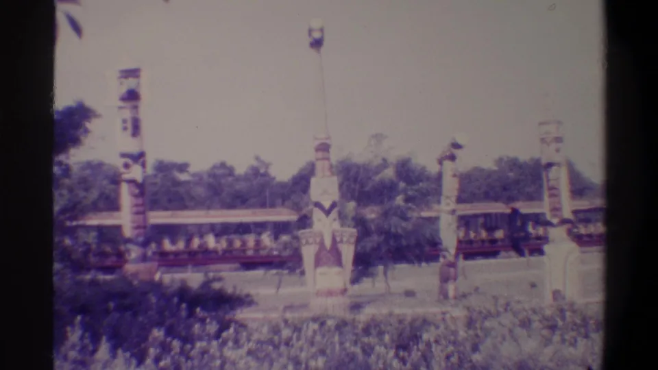 8mm frame from a 1974 Florida family attraction with a carved totem-style pole in the foreground and a slow ride train passing behind.