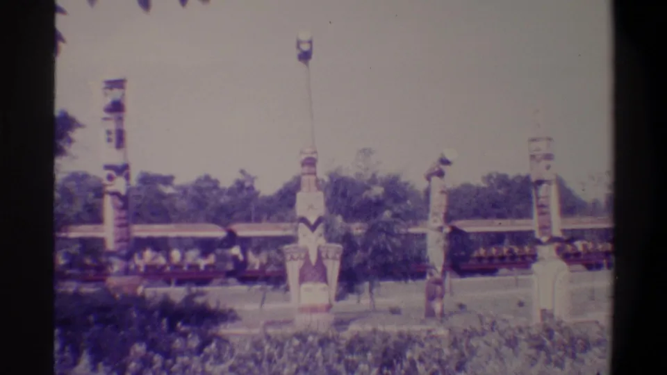 Visitor-shot 8mm frame from a Florida tourist attraction, c. 1974, showing painted totem poles and a passing open-air ride train with passengers.