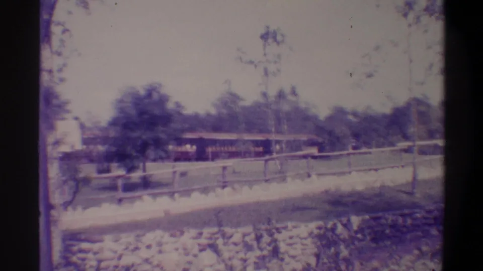 8mm tourist footage from Florida, c. 1974, showing the ride train clearing the totem pole area with stone-edged track and wooden fence in foreground.