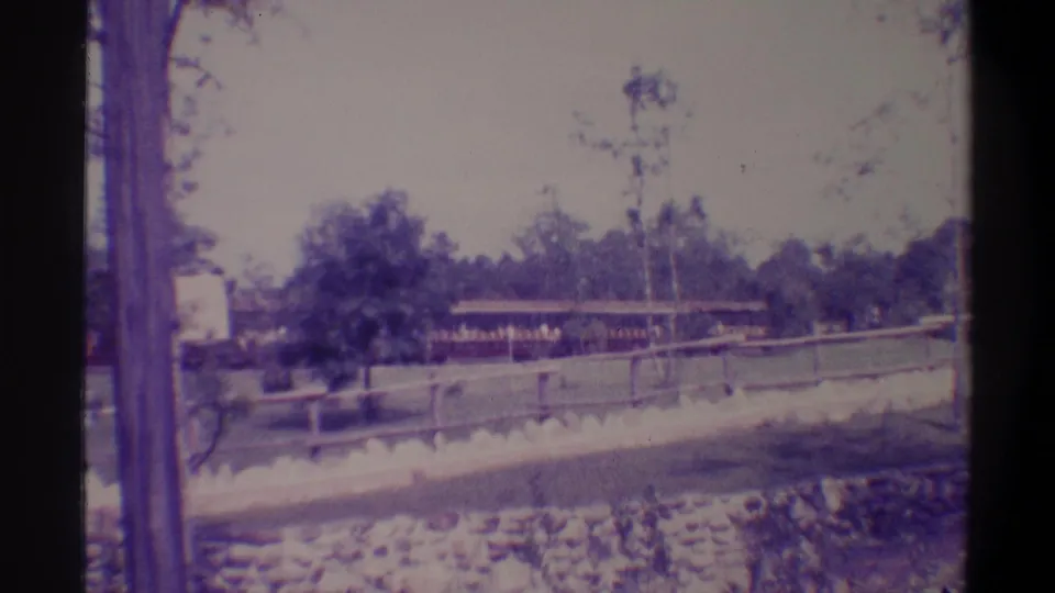 Wide-angle 8mm tourist frame from Florida, c. 1974, as the ride train recedes past the attraction grounds with rock edging and wooden fence visible.