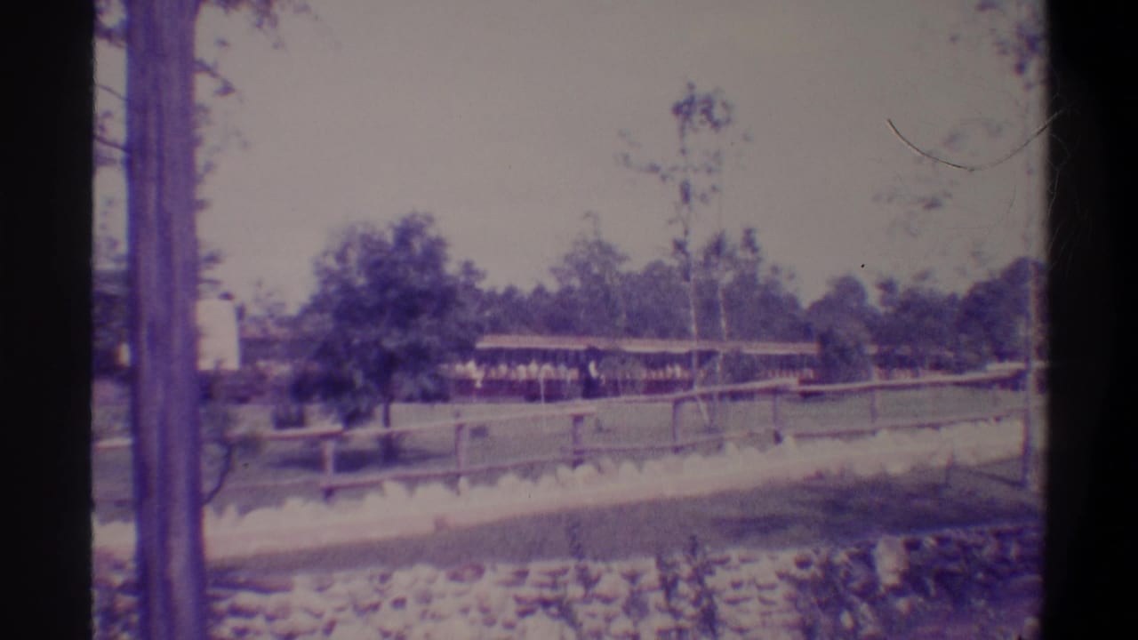 Wooden dock and low covered shed structure beside a stone-lined waterway, trees and utility pole beyond; 8mm home movie, Gainesville Florida area, circa 1974.