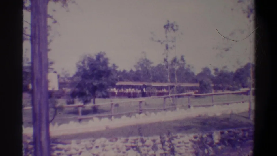 Wooden dock and low covered shed structure beside a stone-lined waterway, trees and utility pole beyond; 8mm home movie, Gainesville Florida area, circa 1974.