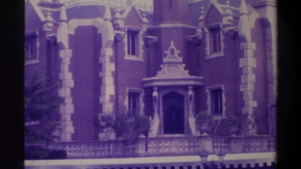 1974 Florida 8mm still showing ground-level entrance of castle-like building with decorative portico, stone trim, potted plantings at base, and pointed dormers above; aged emulsion visible.