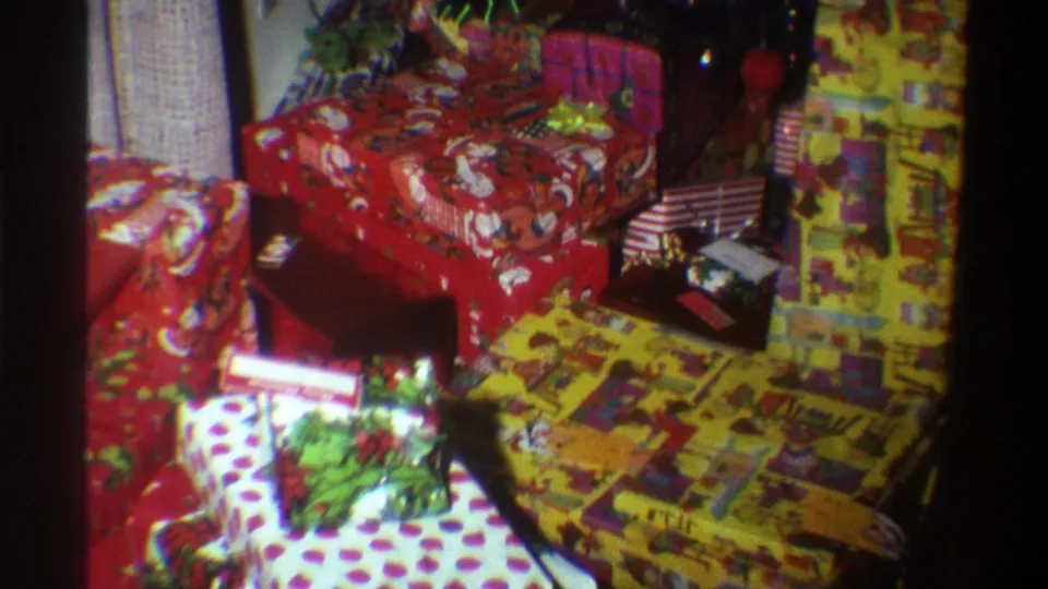 8mm home movie frame circa 1975 showing stacked Christmas gifts in red Santa-print and polka-dot wrapping paper, Gainesville, Florida.
