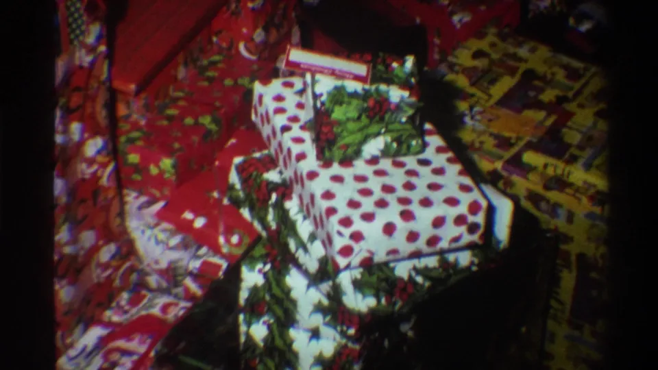 Tighter 8mm frame circa 1975 showing red Christmas-print and white polka-dot wrapped gifts with characteristic mid-1970s film texture.