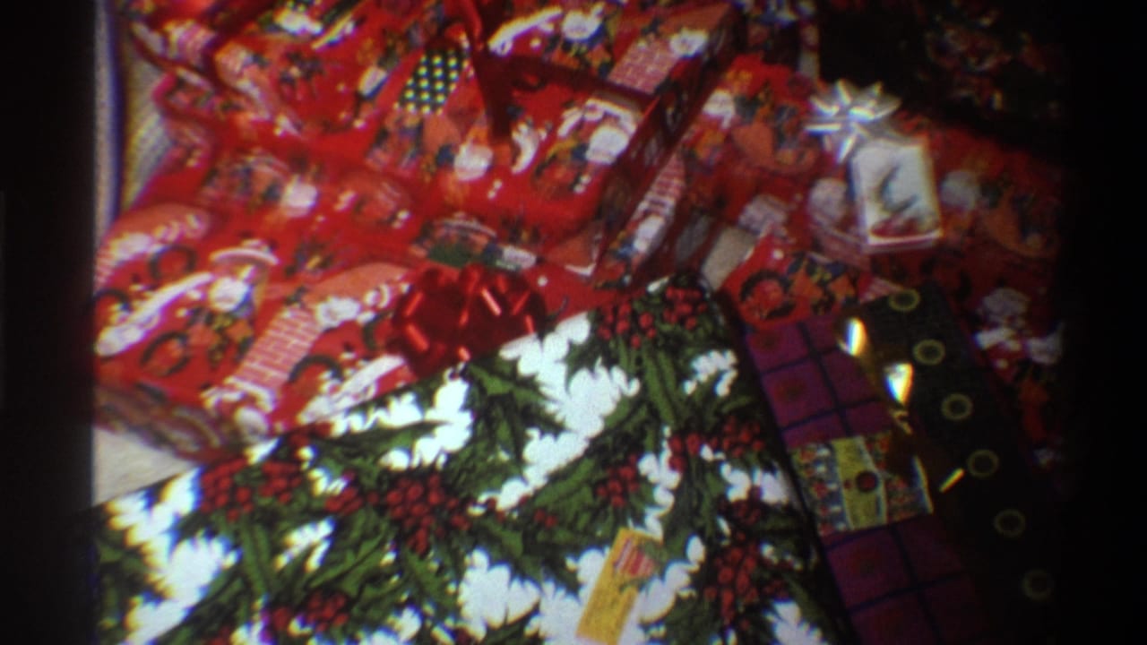 8mm home movie frame from Gainesville, Florida, 1975, showing multiple Christmas presents wrapped in holly-print paper with red and dark accents.
