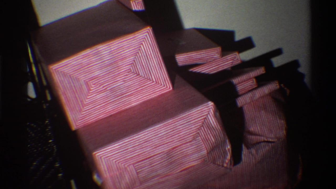 8mm home movie frame from Gainesville, Florida, 1975, showing a neat stack of gifts in red-and-white striped wrapping paper in a dimly lit domestic interior.