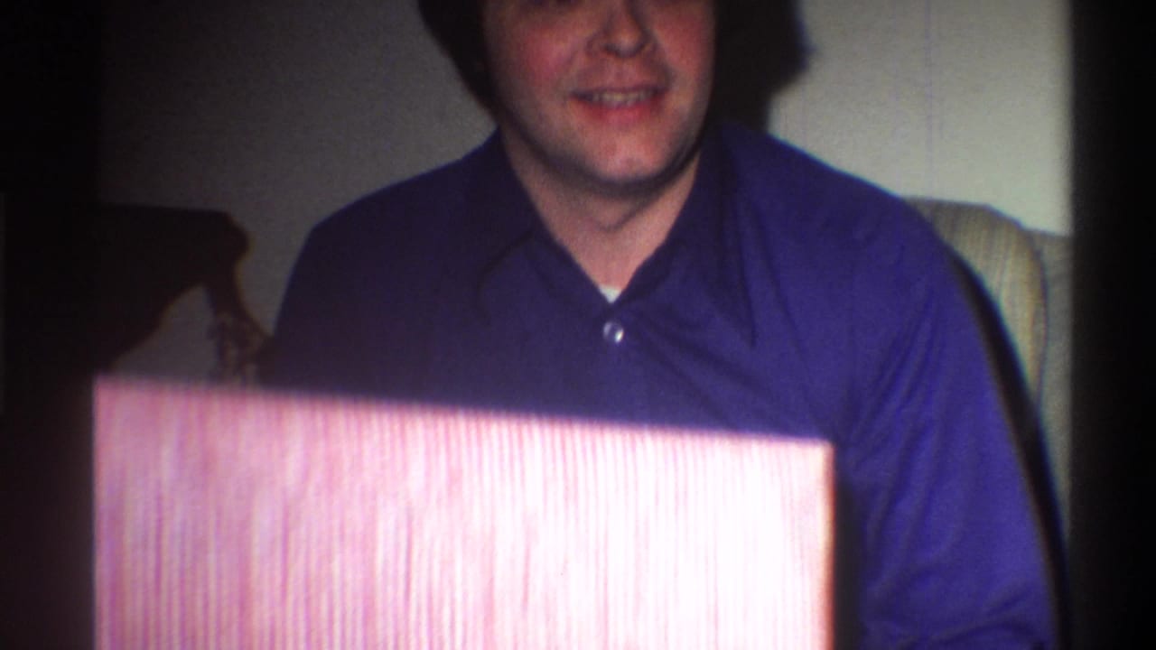 Man in blue shirt holding a large pink-and-white striped wrapped gift box, lower face and torso cropped into frame.