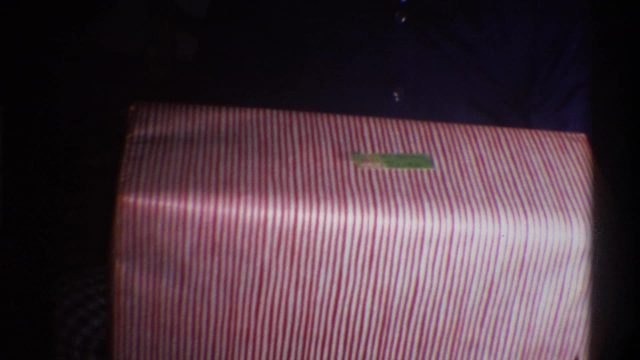 Close-up of pink-and-white striped gift wrapping paper with a small green adhesive label; 8mm home movie, circa 1975, Gainesville, Florida.