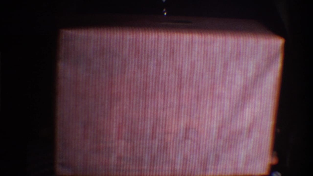 Pink-and-white striped gift box tilted or partially unwrapped, revealing a corner of the inner box; circa 1975 8mm home movie, Gainesville, Florida.