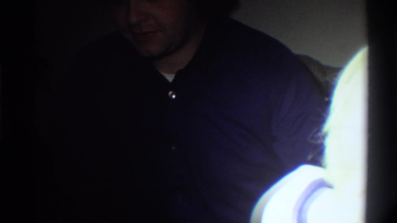 Man in dark shirt bending forward or looking down in a dim home interior, possibly mid-1970s domestic Florida setting