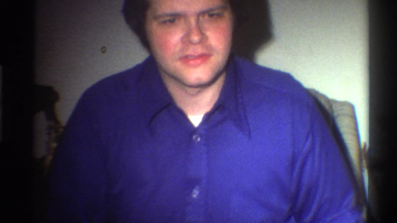 Adult male in blue button-down shirt looking toward camera in a dim domestic interior, Gainesville Florida circa 1975