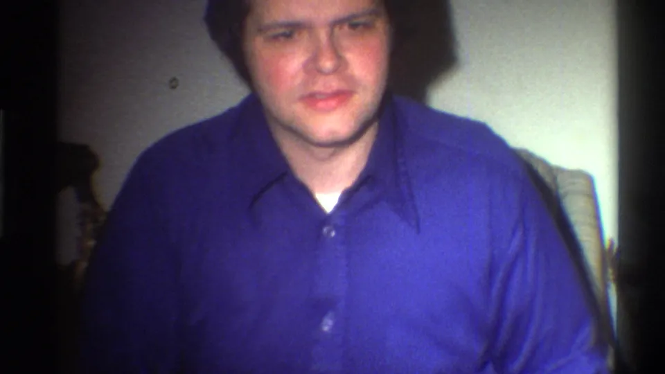 Adult male in blue button-down shirt looking toward camera in a dim domestic interior, Gainesville Florida circa 1975