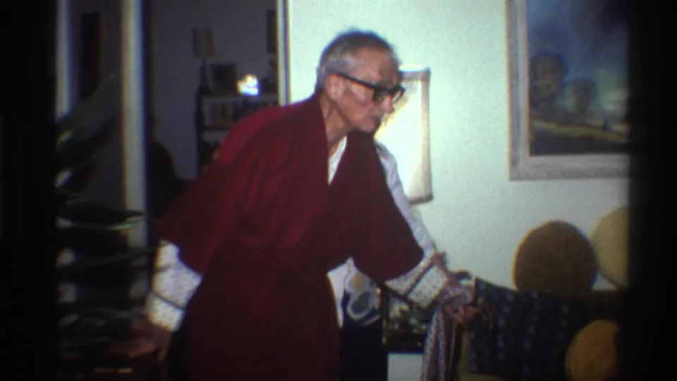 Elderly man wearing glasses and a dark red robe moves through a living room during a Gainesville, Florida family Christmas gathering, circa 1975.