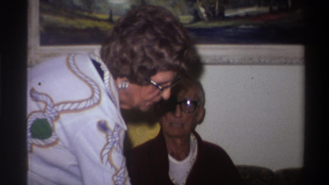 Two women in a 1975 Gainesville Florida home movie; the standing woman's embroidered white sweater and voluminous curly hair place the clip in mid-1970s domestic Americana.