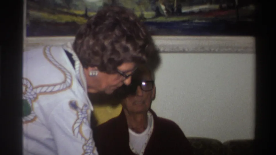 Third frame from a 1975 Florida home movie; the framed landscape painting is more prominent in the upper portion of the frame and the older woman looks downward.