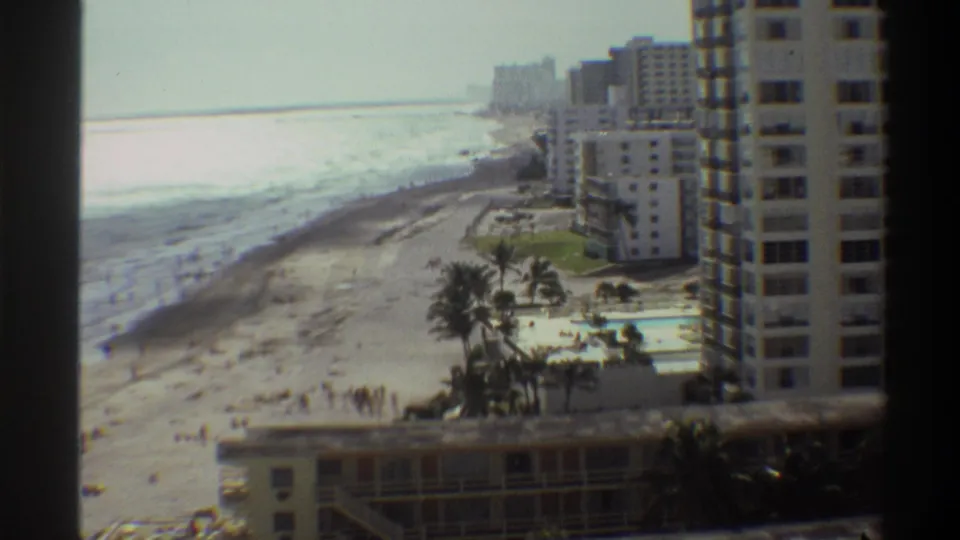 8mm footage of Florida beachfront high-rise hotels and a poolside courtyard with palm trees, circa 1975, shot from an adjacent elevated position.