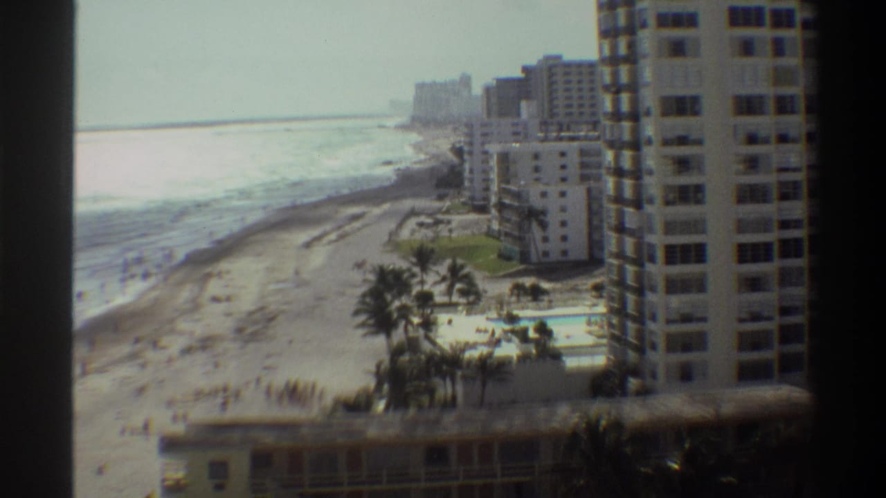 High vantage-point 8mm home movie circa 1975 of a Florida coastal resort, showing high-rise apartment towers, palm trees, a pool, and beach.